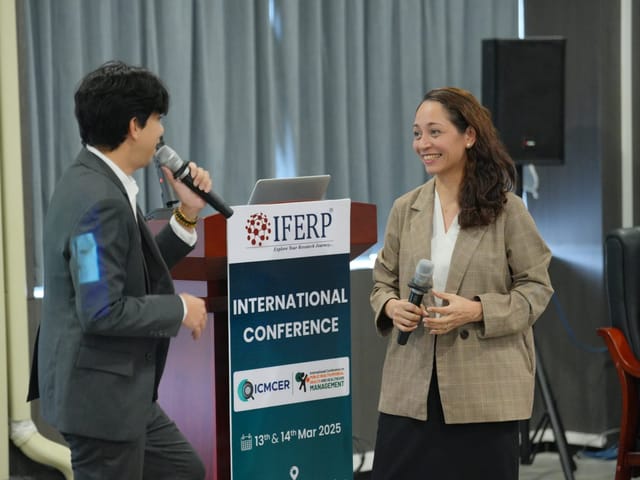 Two speakers with microphones beside an IFERP lectern during an international conference session